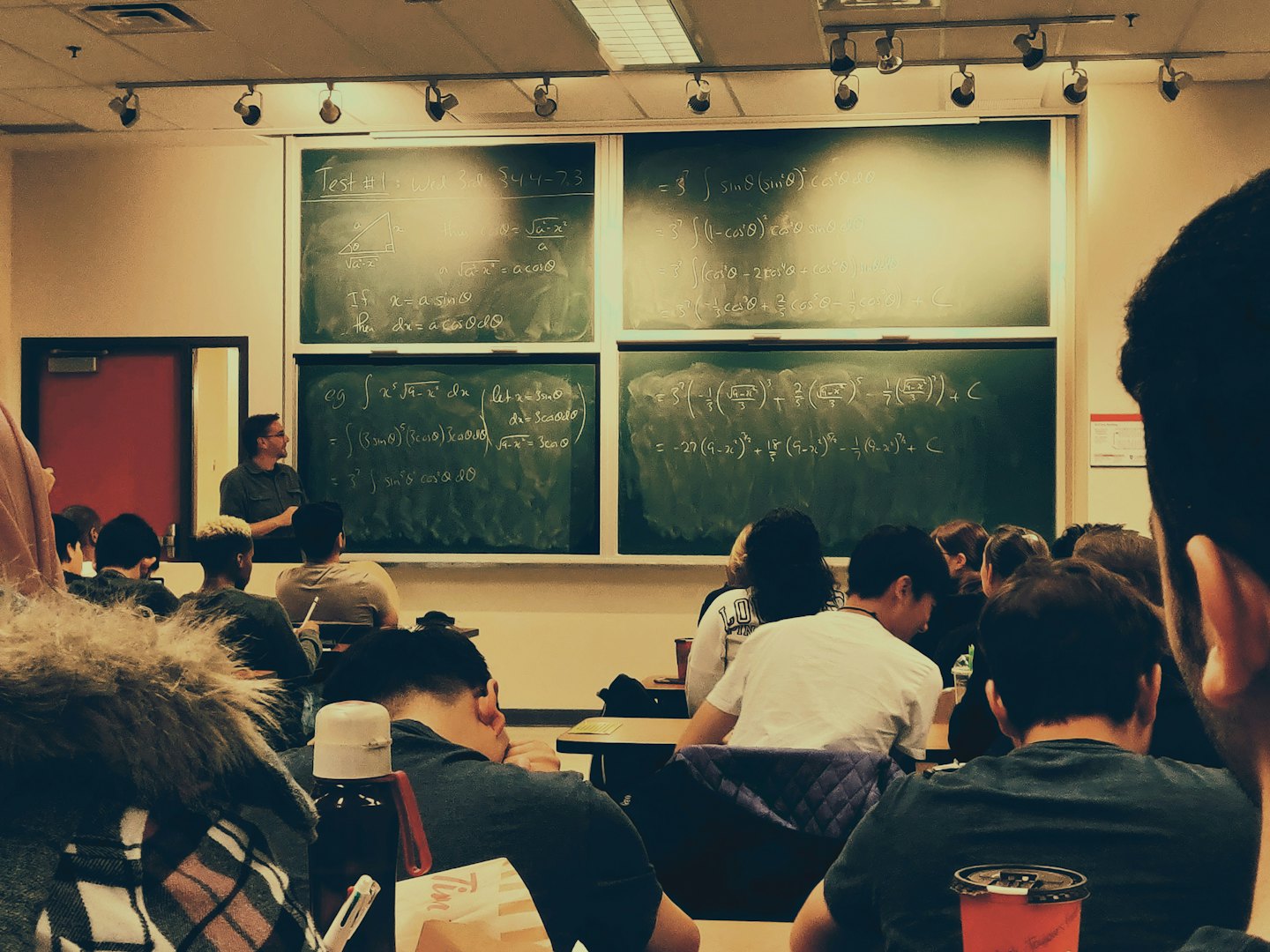 Teacher at blackboard lecturing diverse students in a math class.